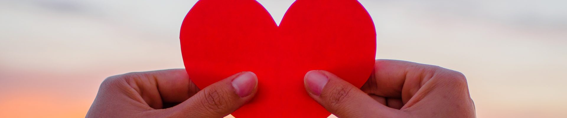 hand is raising the red paper heart with blur sunlight during sunset, Valentines day