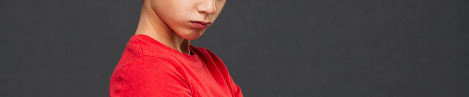 Photo of angry little boy child standing isolated over grey background. Looking camera with arms crossed.
