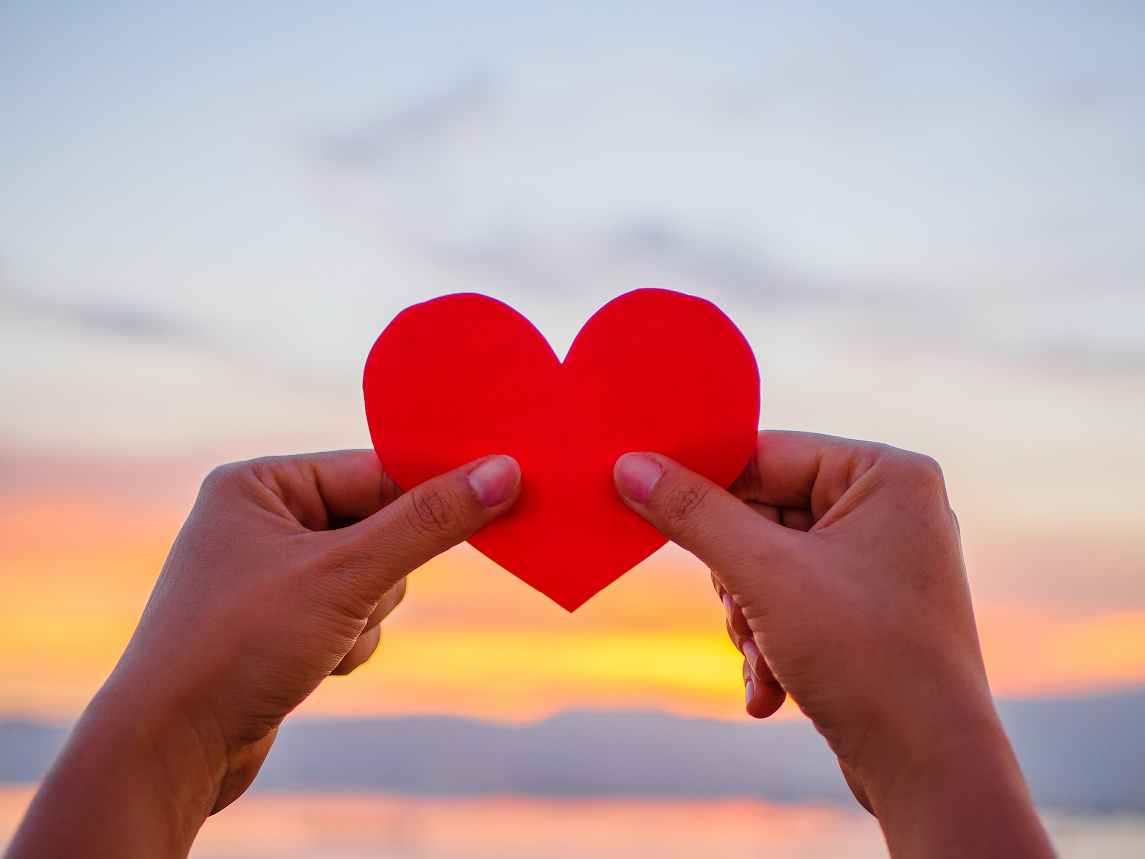 hand is raising the red paper heart with blur sunlight during sunset, Valentines day